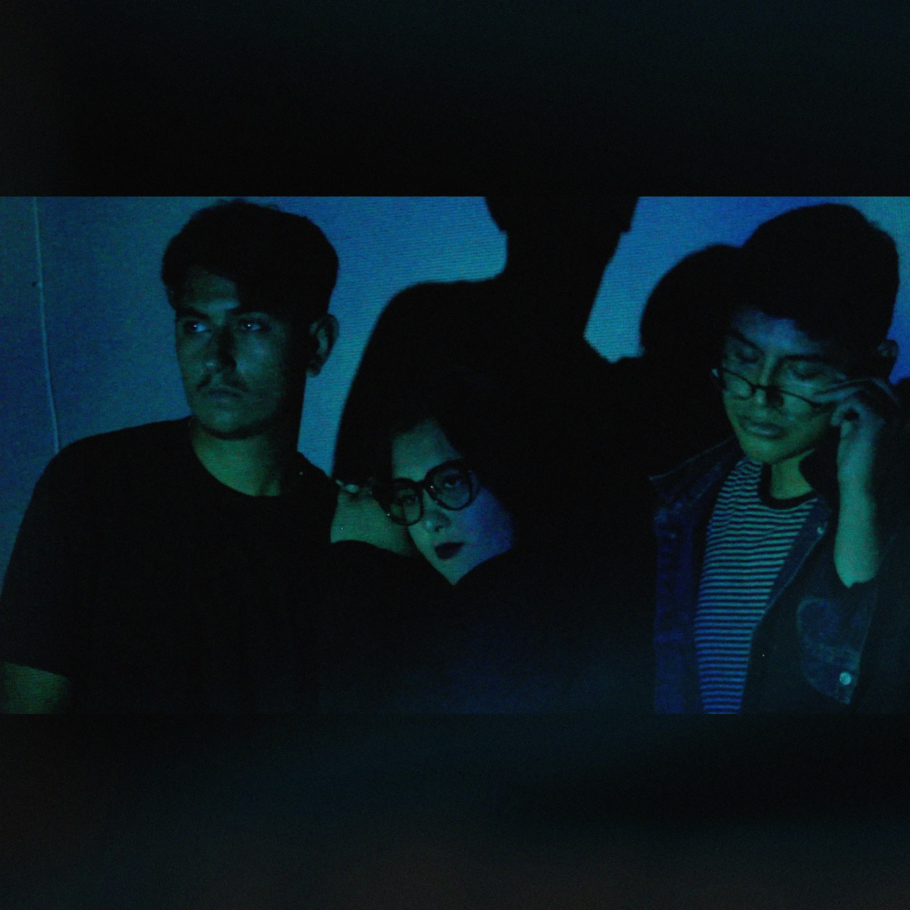 Artwork for The Modes' single, Fly. The picture shows the three members of the band in a dark room. Jesus and Aziza are looking away; Aziza is resting on Jesus's shoulder. Tom is looking down while holding his glasses.